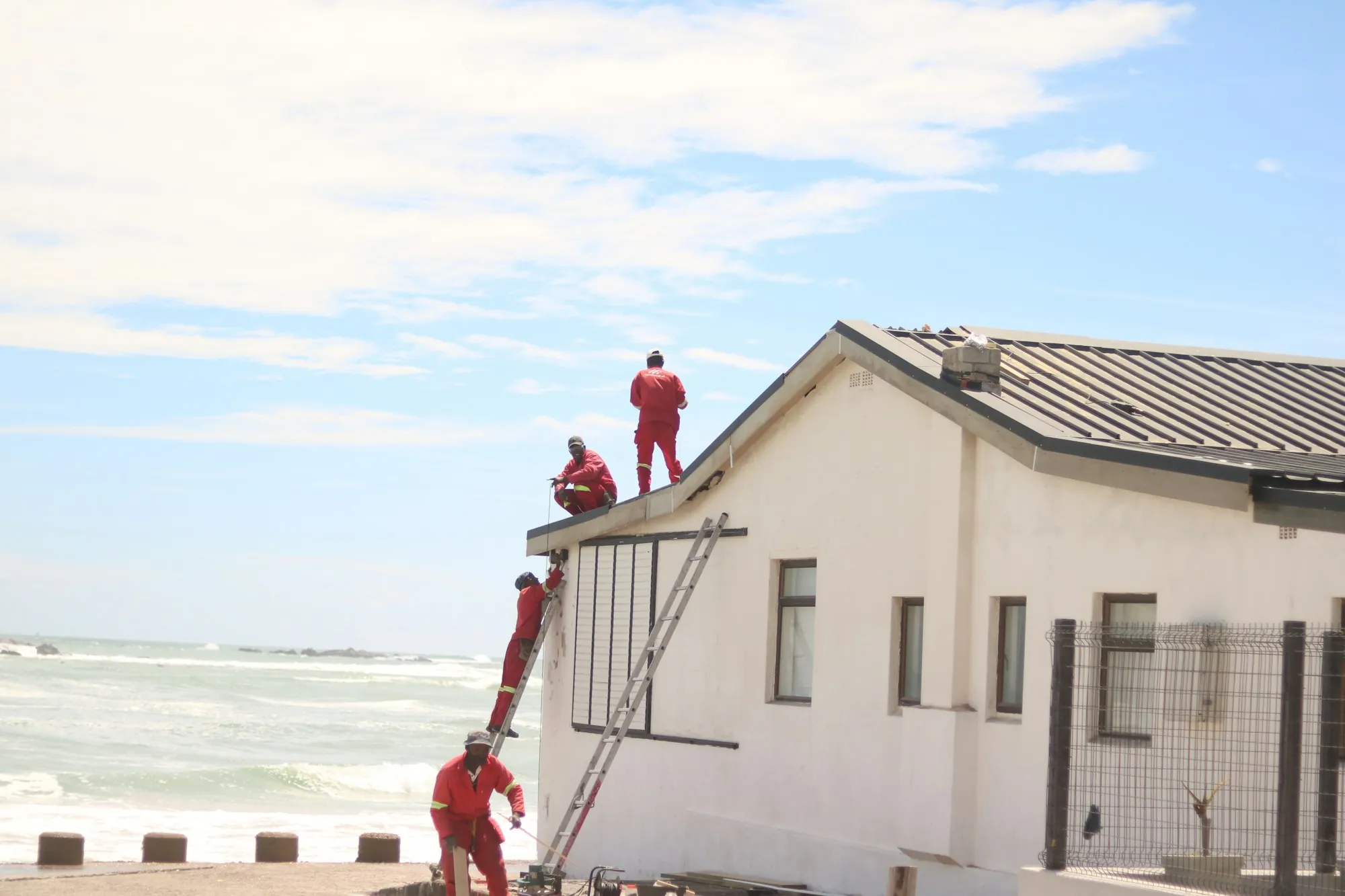Workers on ladders repairing the roof of a white building