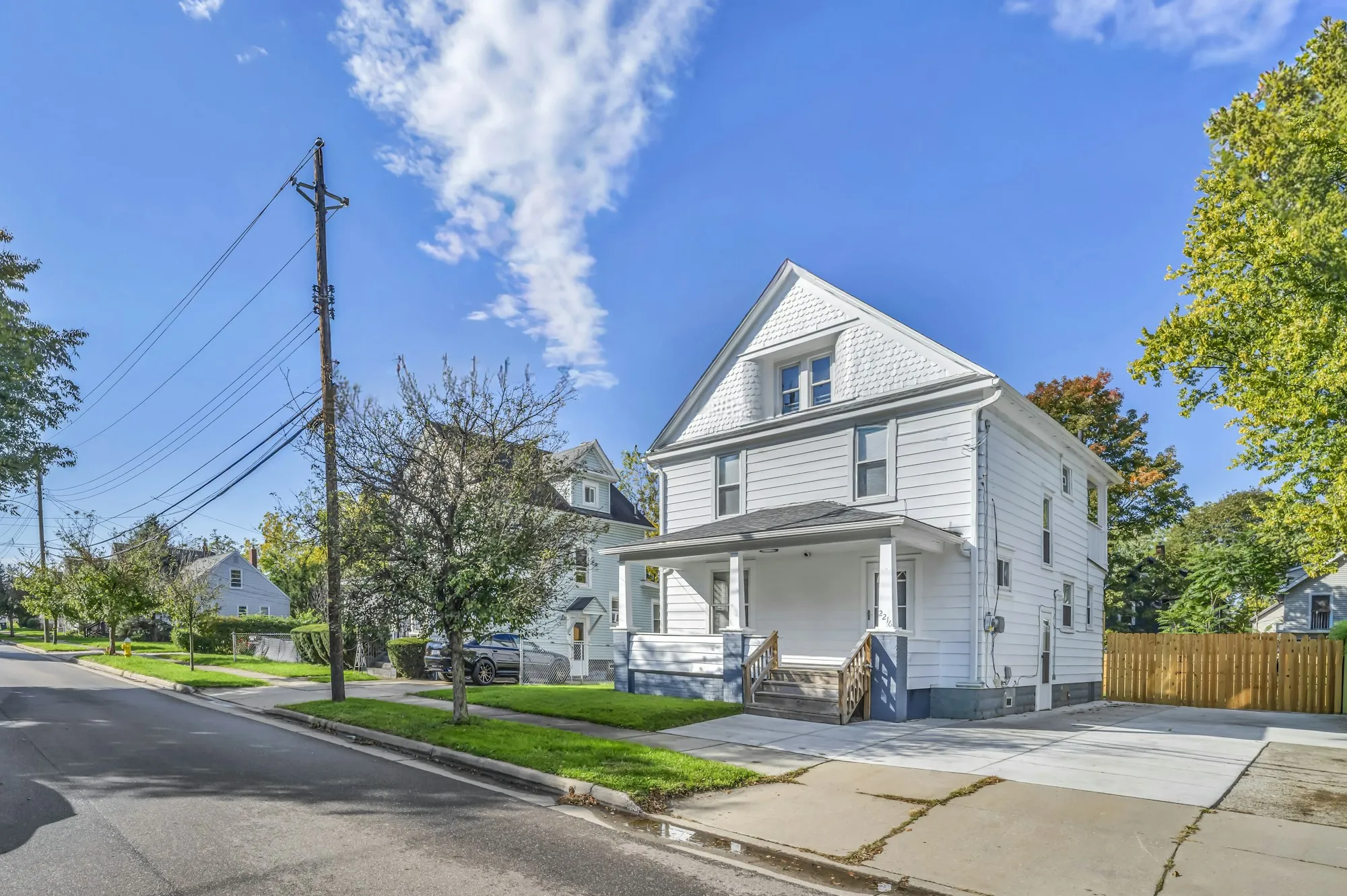 White two-story home with a gray shingle roof on a sunny residential street