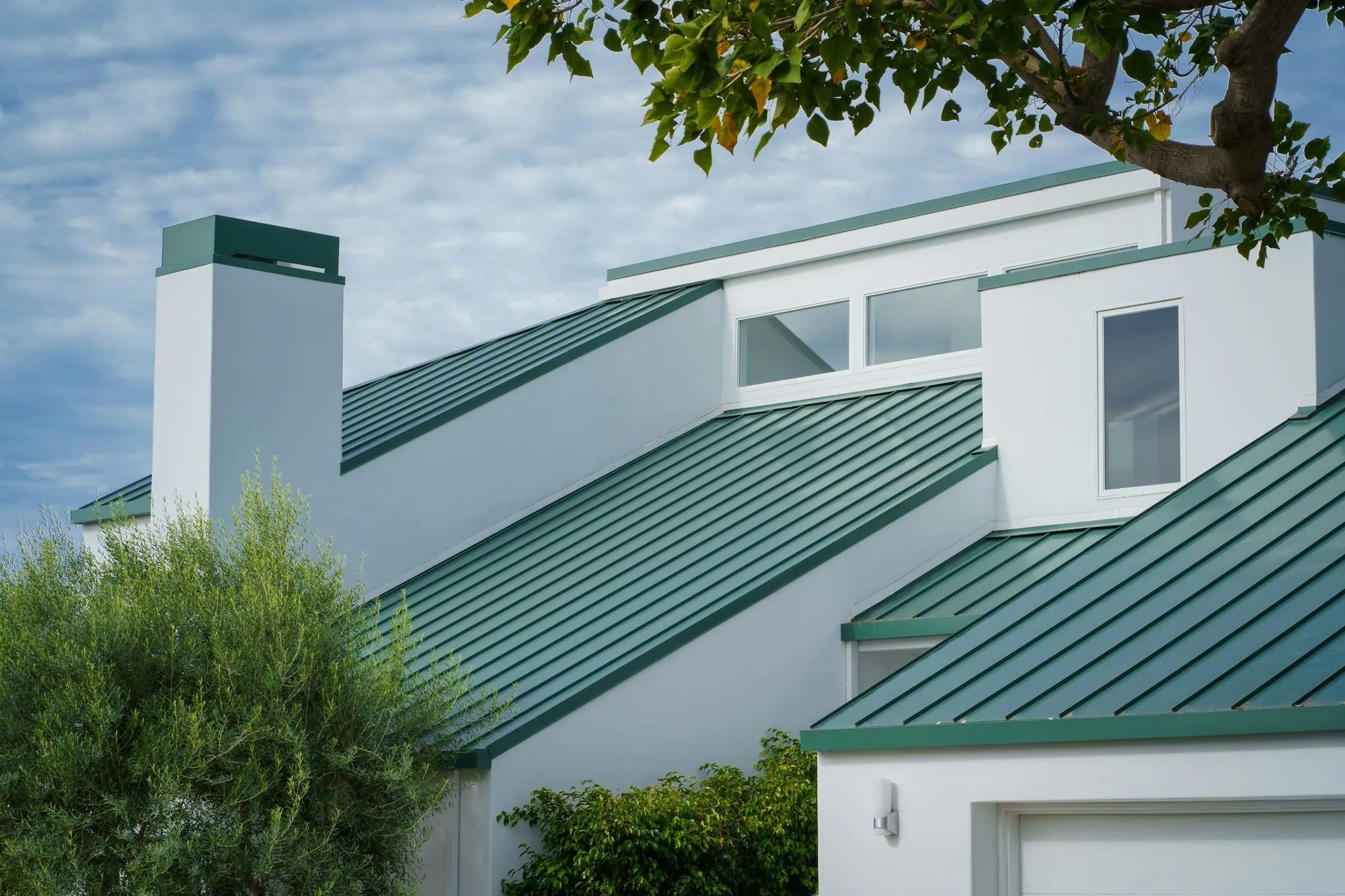 Green standing seam metal roofs on a white house with a chimney