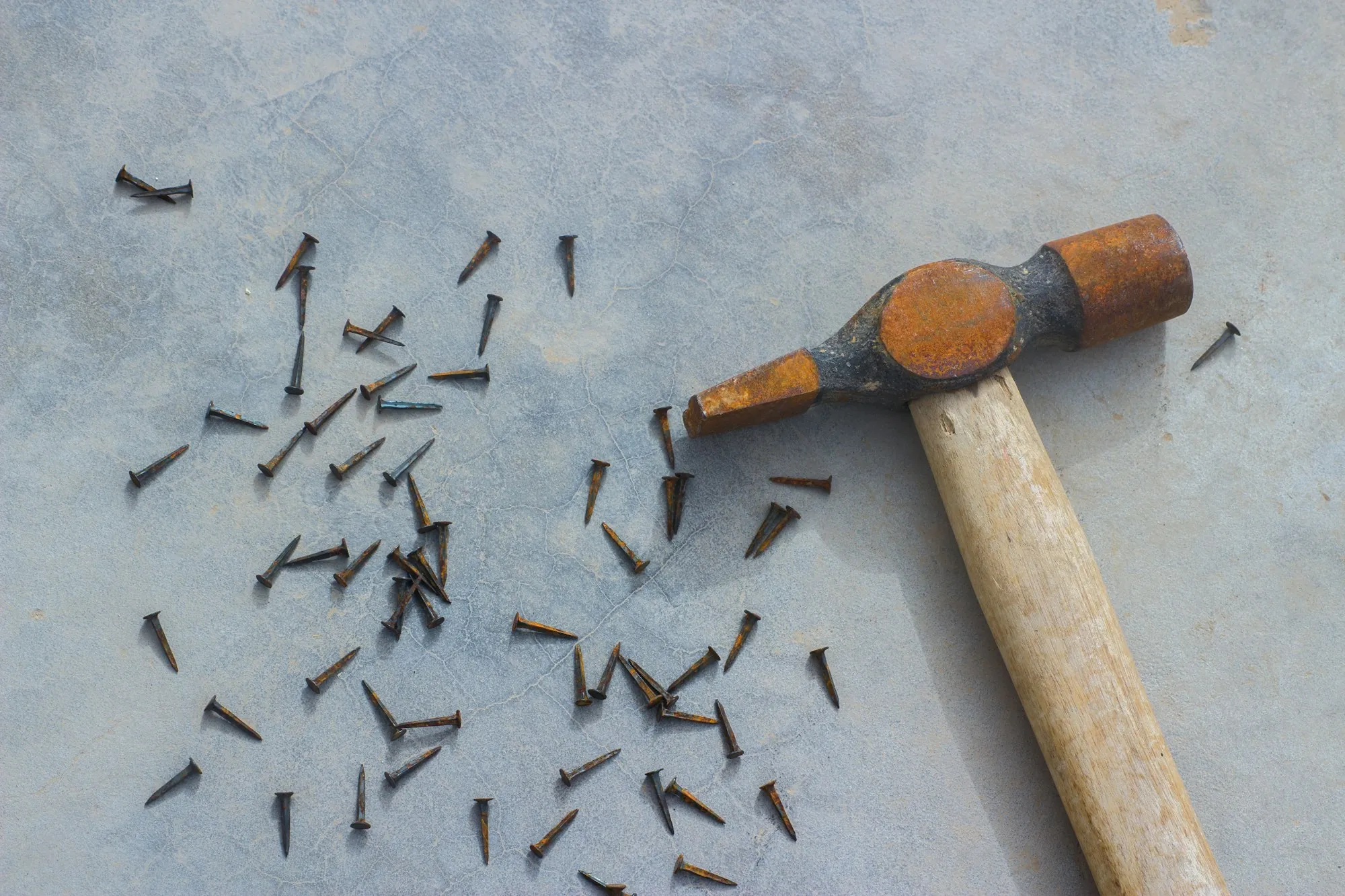 Wooden-handled hammer with loose nails on a gray surface